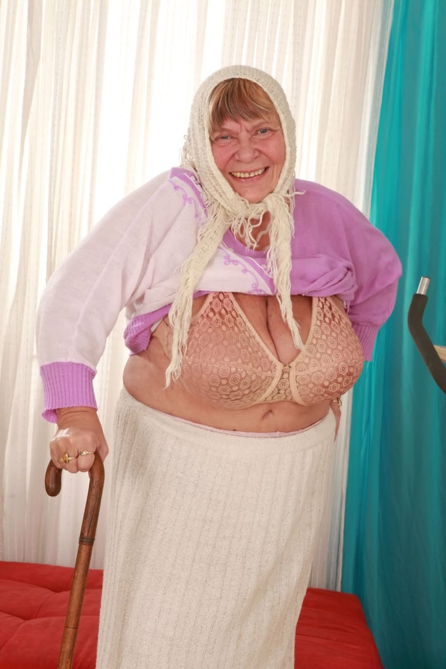 Old granny Sara G in skirt & boots sheds sweater to show huge tits in bra