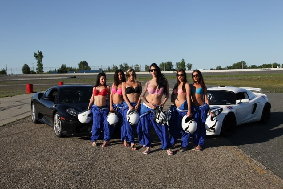 Race poses seductively with other busty racers baring big tits by sleek race cars - 2