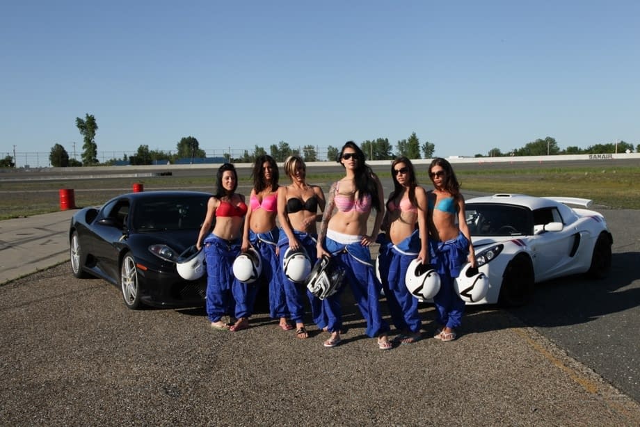 Race poses seductively with other busty racers baring big tits by sleek race cars - 3