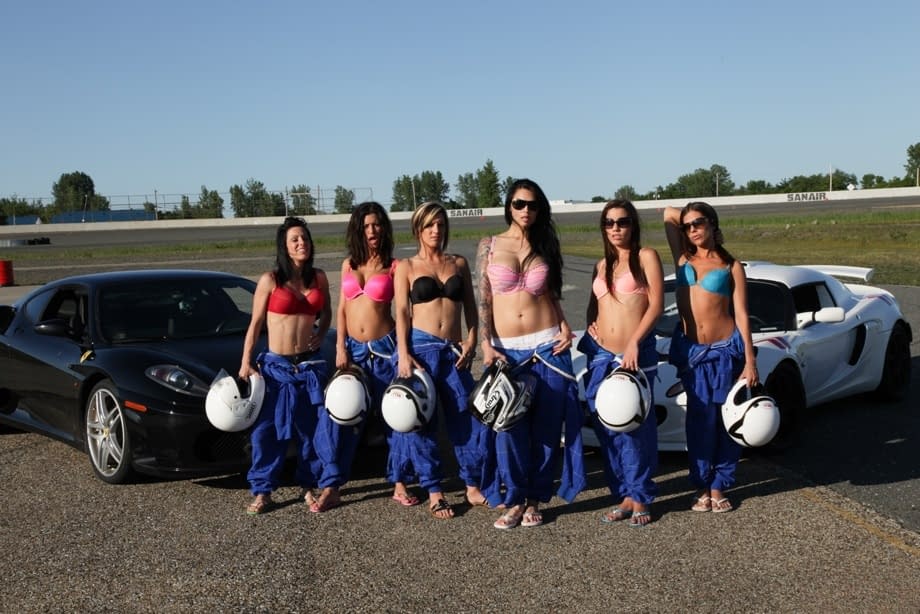 Race poses seductively with other busty racers baring big tits by sleek race cars - 5