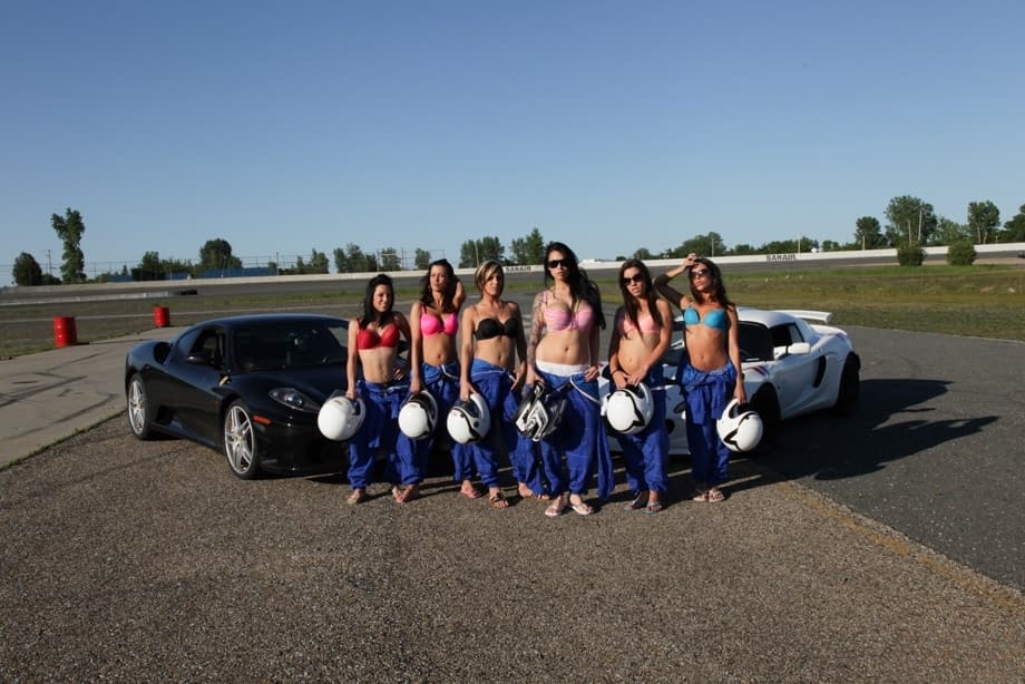 Race poses seductively with other busty racers baring big tits by sleek race cars - 6