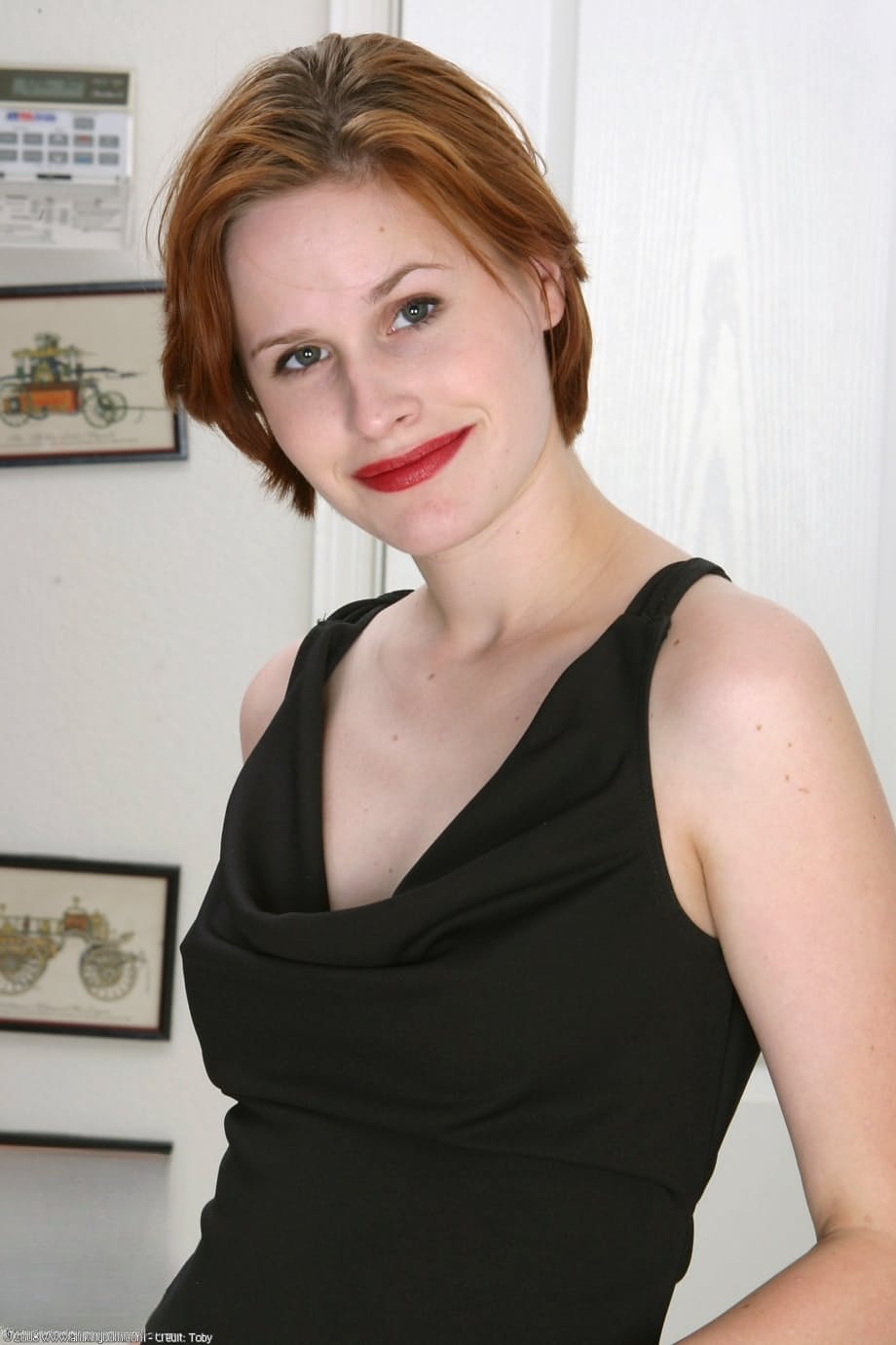 Fair skinned redhead with red lips slips off a black dress to pose nude